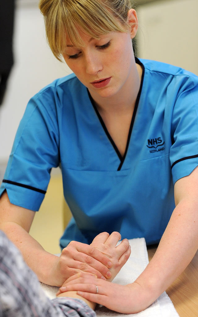 Nurse holding and examining patient's hand. Patient's hand resting on table.